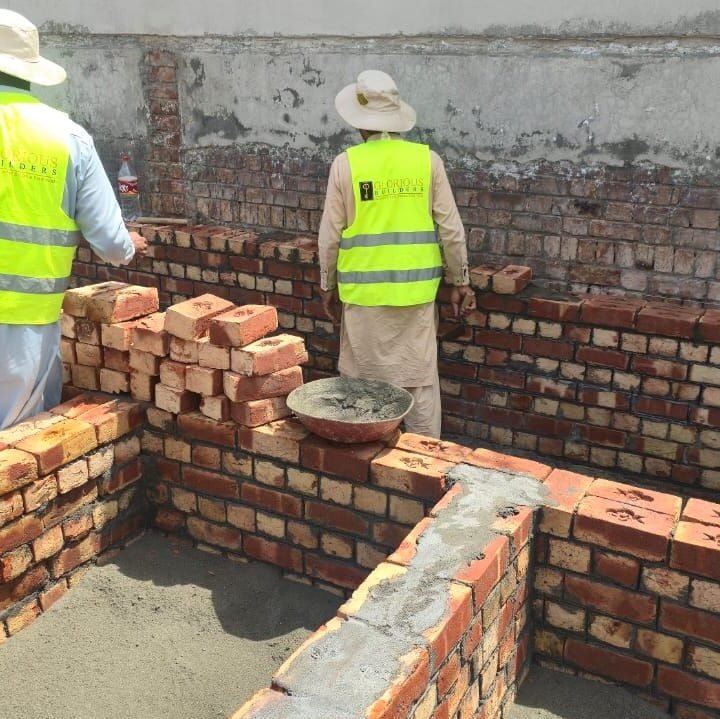 Two workers in safety vests building brick walls at a house construction site in DHA Lahore