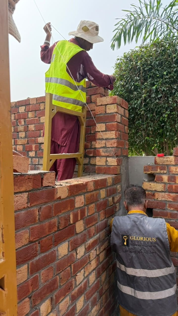 Two workers laying bricks on a yellow steel scaffold at a residential building site in Lahore