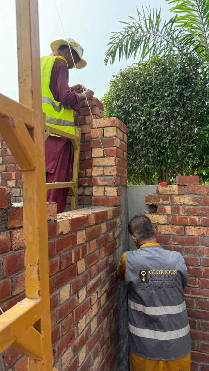 Mason working on a brick wall with steel scaffold during residential construction in Lahore