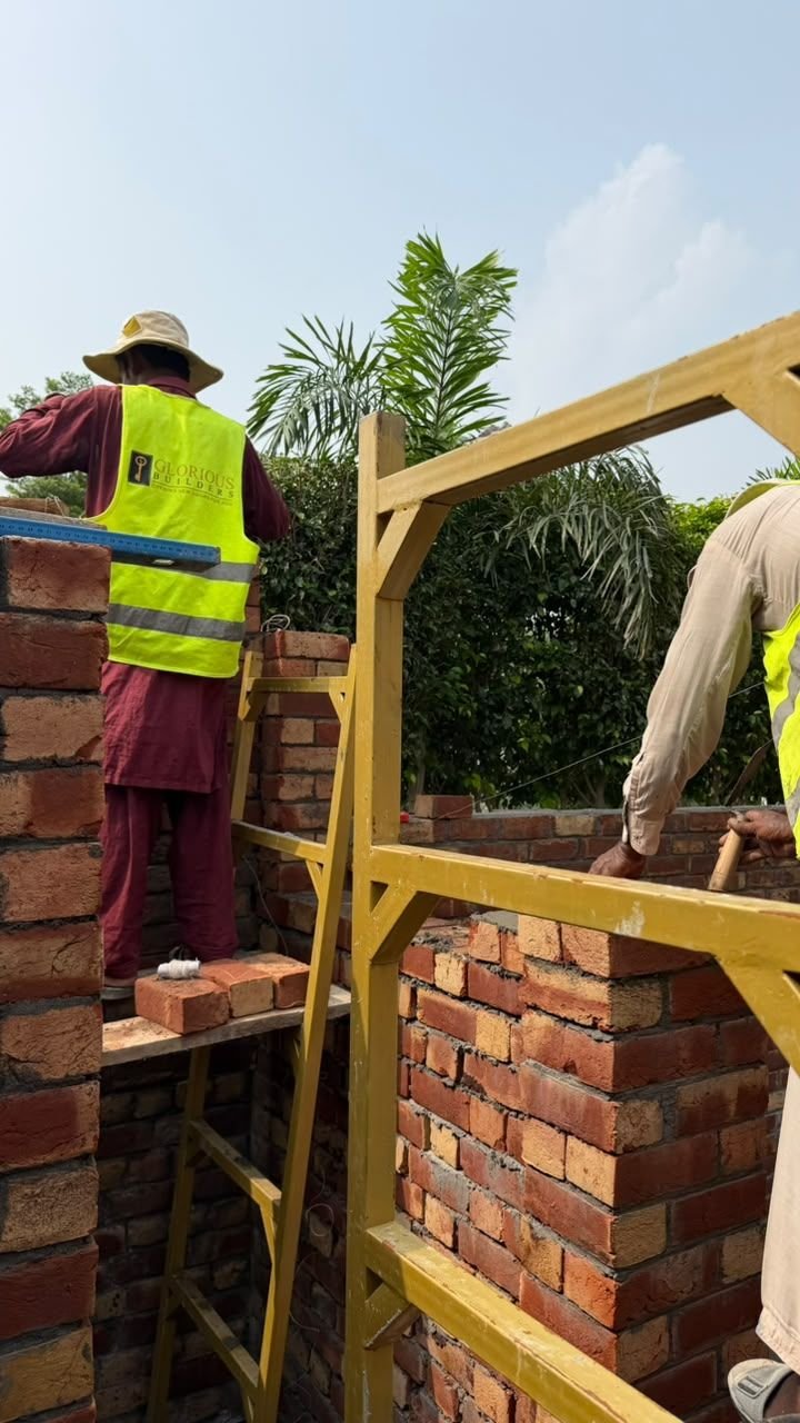 Labourer laying bricks inside a yellow scaffold frame on a house construction site in Lahore