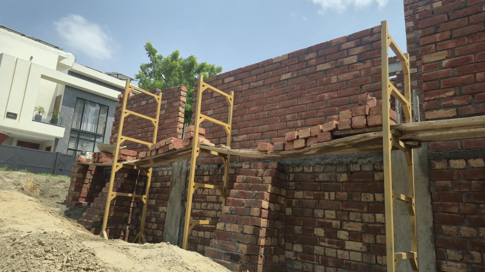Brick wall with yellow scaffolding next to a neighbouring house under construction in Lahore