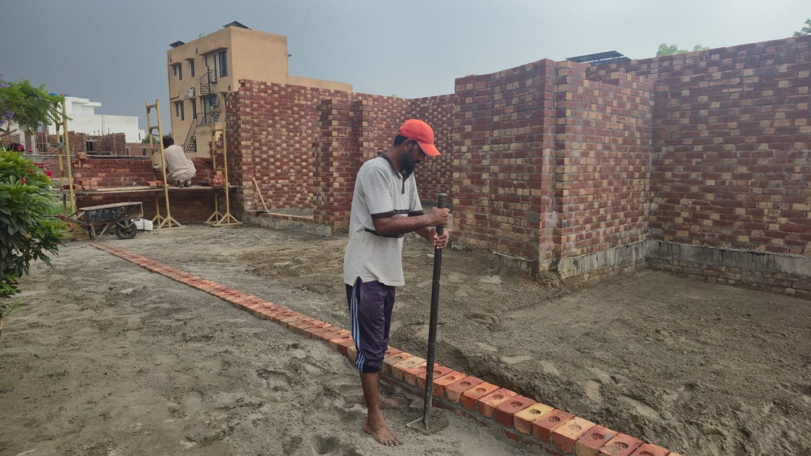 Labourer levelling soil beside a new brick wall at a residential construction site in Lahore