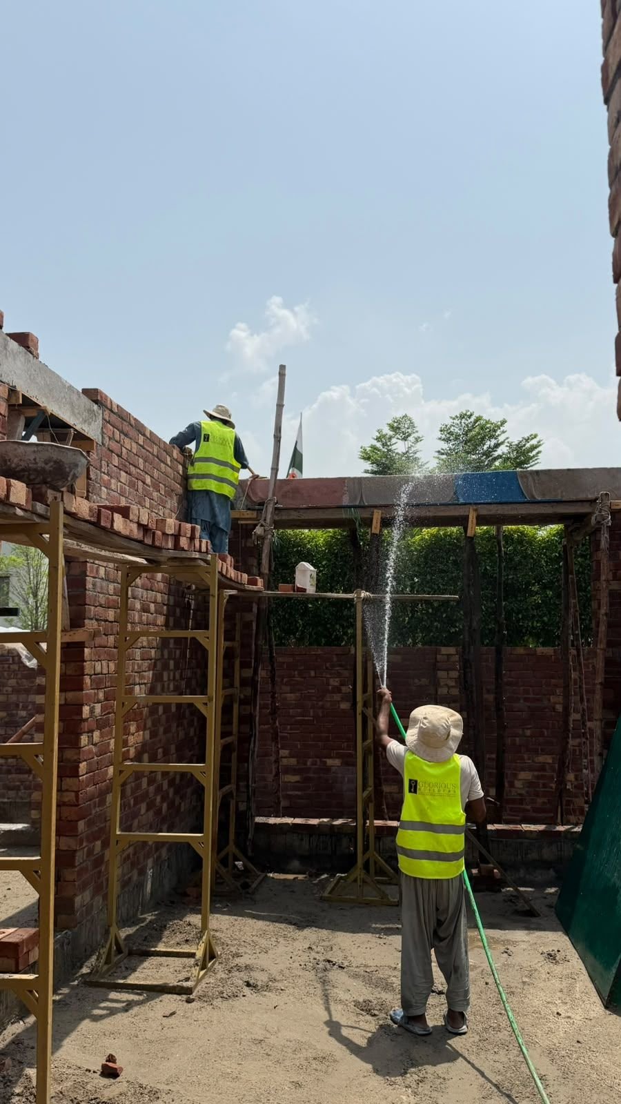 Worker curing fresh brick work with a water hose at a house construction site in Lahore