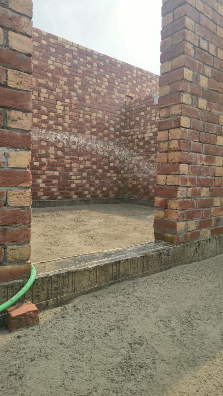 Water curing of brick wall and plinth with a hose at a house construction site in Lahore