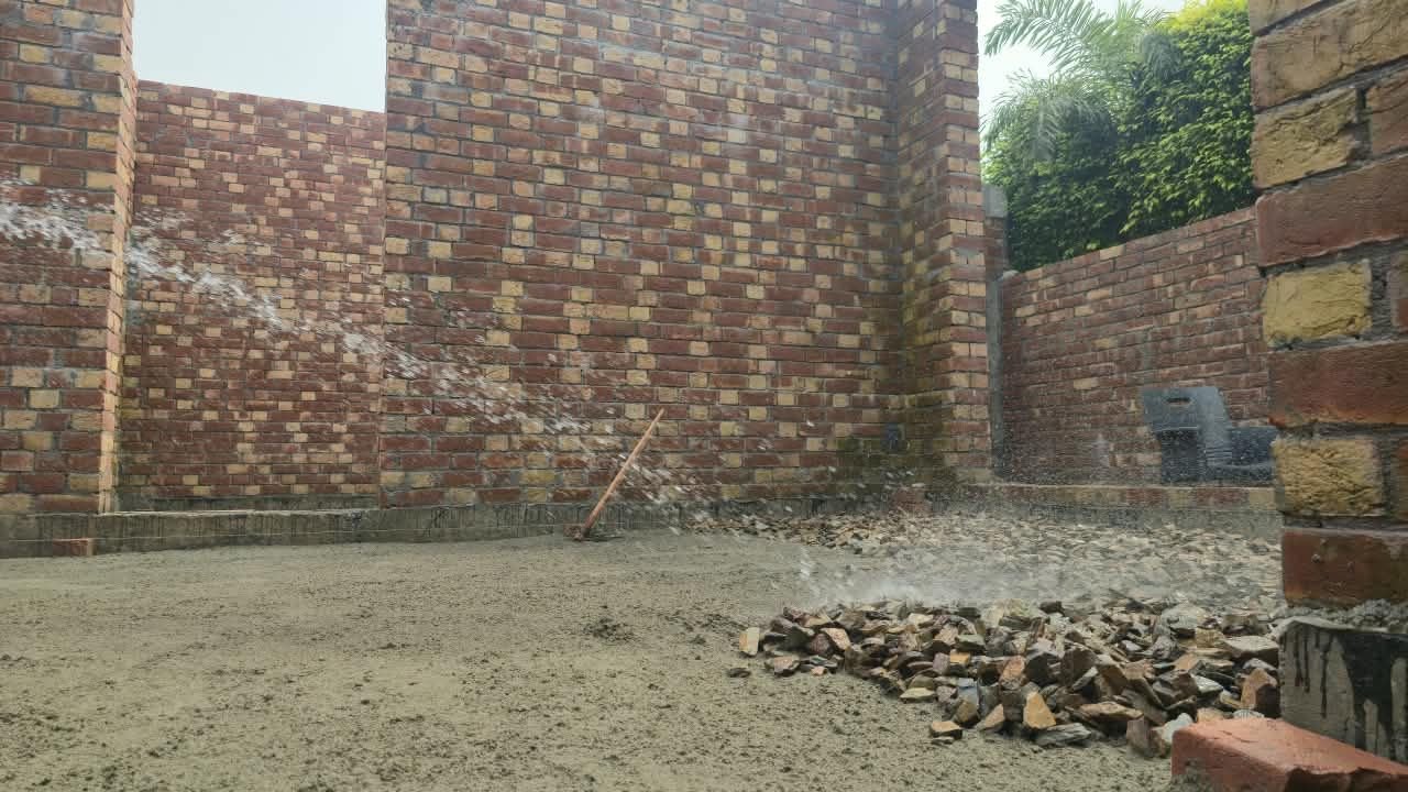 Sprinkling water for curing on a brick wall at a house construction site in Lahore