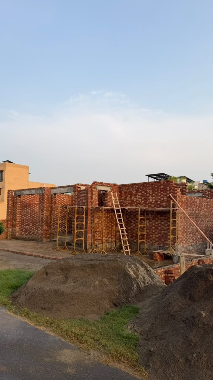 Wide view of a house under construction with brick walls and scaffolding in Lahore