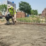 Worker compacting soil with a plate compactor before plinth filling at a house construction site in Lahore