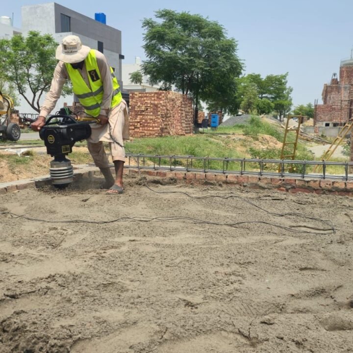 Worker compacting soil with a plate compactor before plinth filling at a house construction site in Lahore