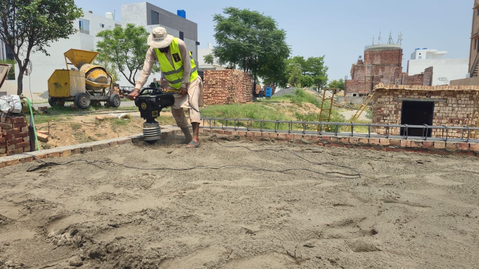 Worker compacting soil with a plate compactor before plinth filling at a house construction site in Lahore