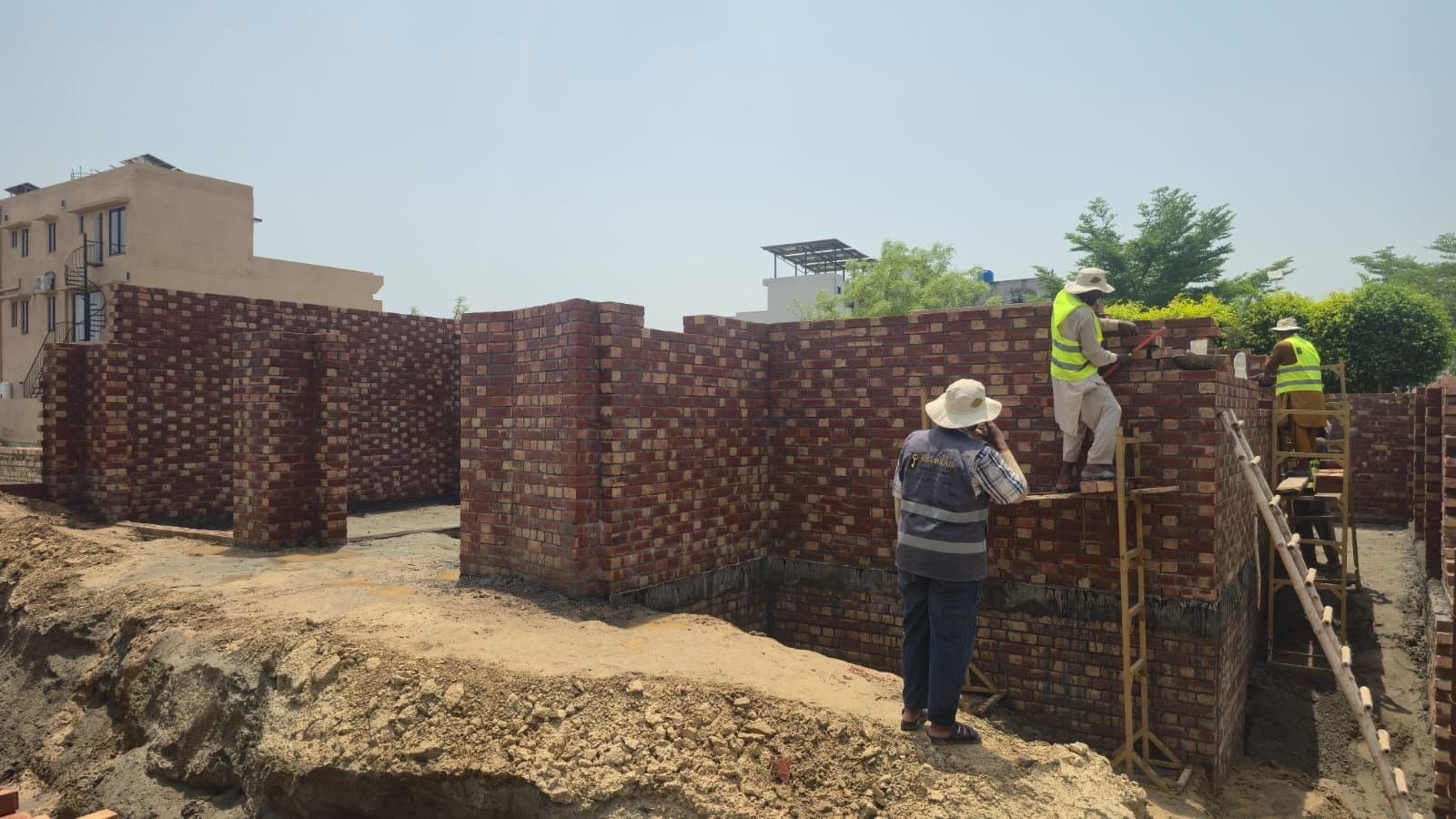 Brick walls rising with workers in safety vests at a house under construction in Lake City Lahore